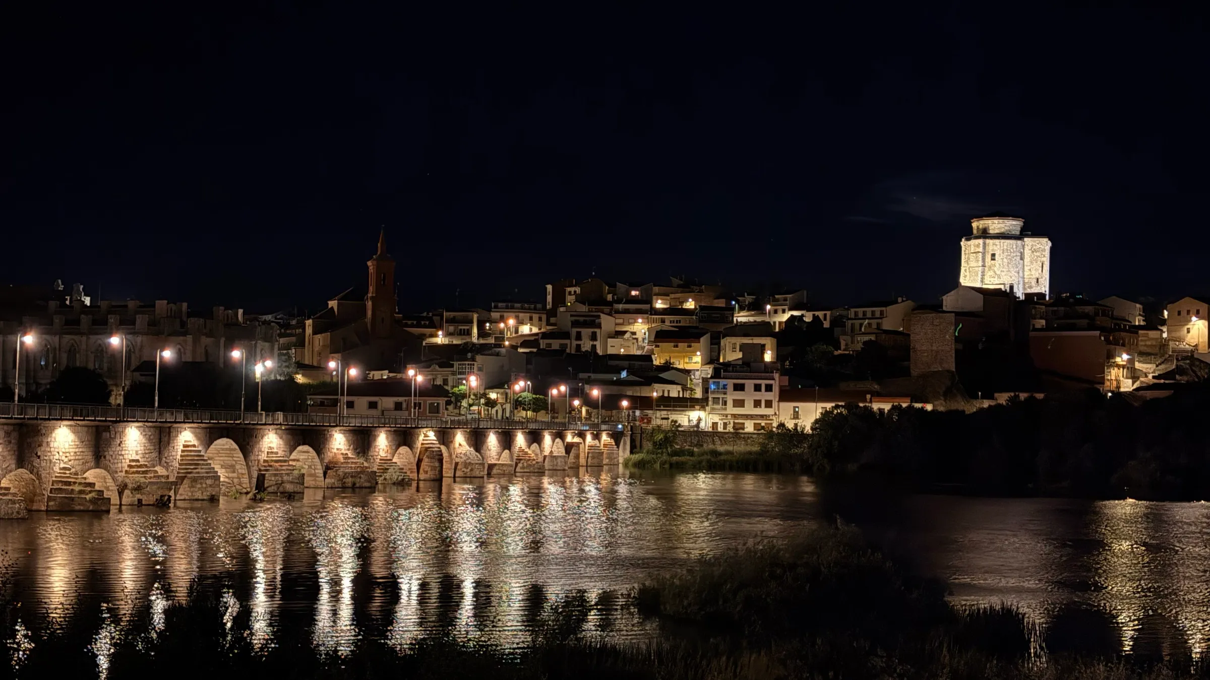 Alba de Tormes de noche: el puente medieval y el castillo iluminados reflejados en el río