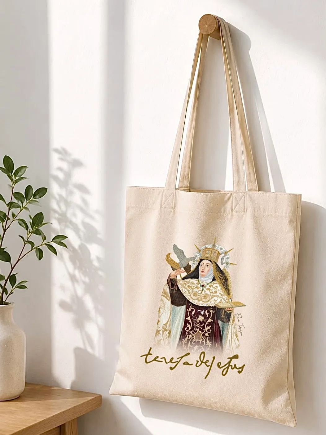 Totebag con la imagen coronada de Santa Teresa de Jesús, colgada en un recibidor junto a una planta