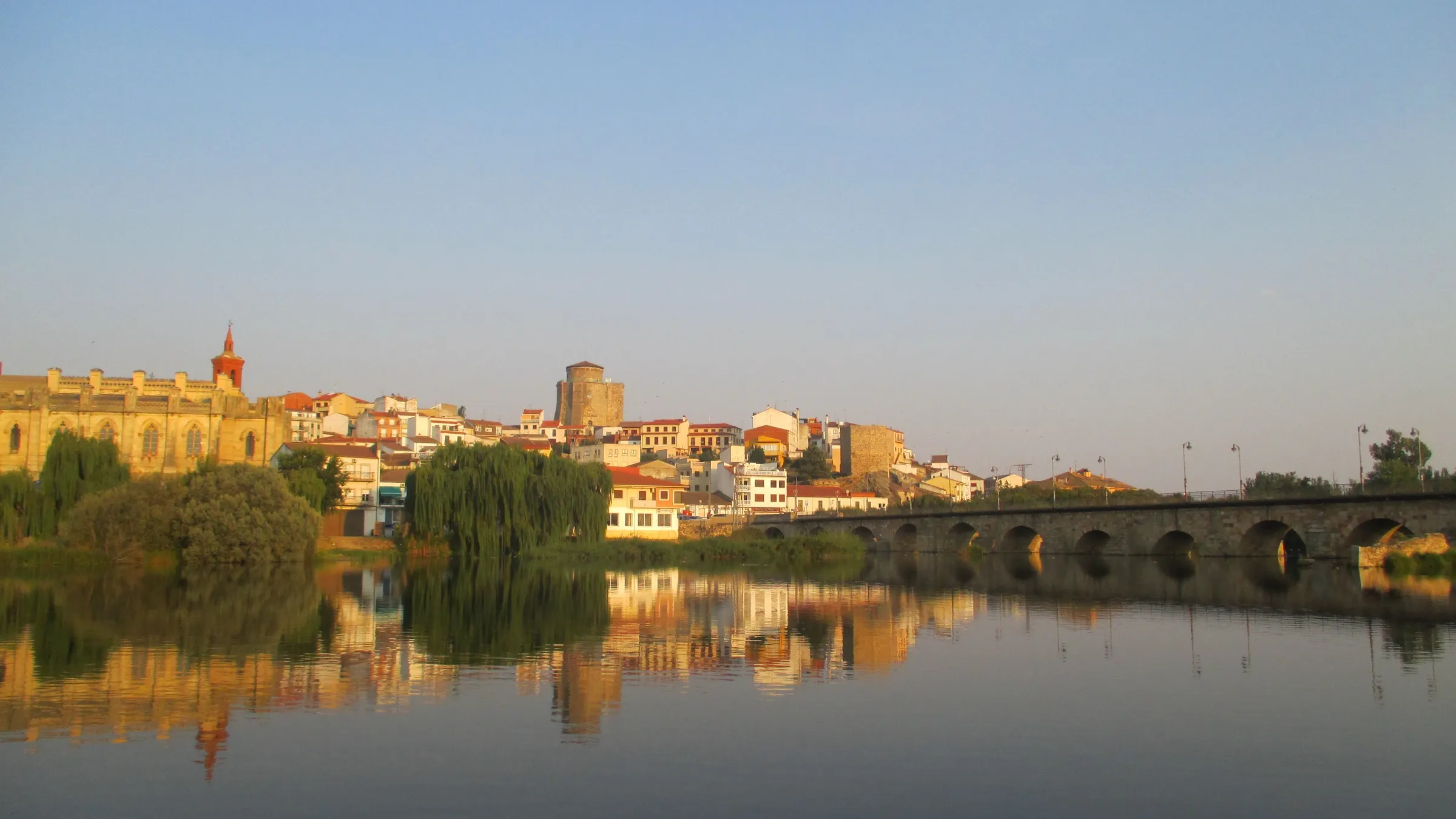 Vista de Alba de Tormes desde el río: la Basílica de Santa Teresa, la torre del Castillo de los Duques y el puente medieval reflejados en el Tormes